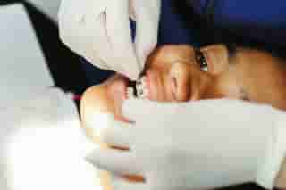 An orthodontist in white latex gloves fits a wire to a fixed metal brace